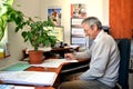 Old man with smile, an accountant, sit in office and works with pen in his hand. On the table are many documents.