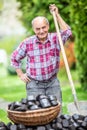 Old man smiling, leaning against a spade next to a pile of coal briquettes with a basket full of them in front of him Royalty Free Stock Photo