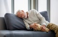 Old man suffering from knee pain lying on sofa in the living room, Elderly man suffering from headache while sitting on the sofa Royalty Free Stock Photo