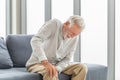 Old man suffering from knee pain sitting sofa in the living room, Elderly man suffering from knee pain while sitting on the sofa Royalty Free Stock Photo