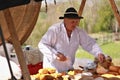 An old man in traditional clothing sells cheeses at a street market.