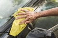 An old man uses a yellow washcloth to clean the B-pillar of his black hatchback. A car owner cleaning and taking care of his auto