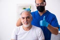 Old man visiting young male doctor in hair transplantation conce Royalty Free Stock Photo