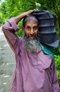 Old man walking on the muddy ground with a heavy load on his shoulder. Old man with beard and moustache