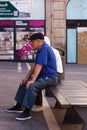 An old man wearing a blue shirt sitting on a bench i