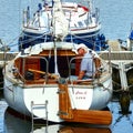 Old man with white hair sits in his sailboat at the jetty and rests