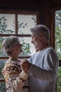 Old man and woman happy couple dancing at home in living room with outdoors background and windows. Senior people enjoy chalet for Royalty Free Stock Photo