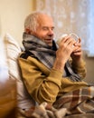 Old man wrapped in blanket has cold and drinks hot infusion