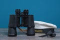 Old marine binoculars and peakless cap on a turquoise background on a textured wooden table