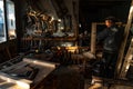 Old master carpenter in grey clothes is getting ready for work in his home workshop, many tools hang on the wall