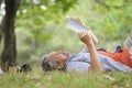 old mature male relax outside in nature garden,happy senior man smile,casual lying on his back on grass reading a book Royalty Free Stock Photo