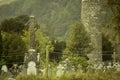 Old medieval Celtic Cross in Glendalough, Ireland. Cemetery in nature, Green forest and tall trees.