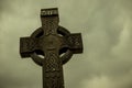Old medieval Celtic Cross in Glendalough, Ireland. Low angle camera with the grey and cloudy sky.