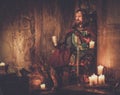 Old medieval king with goblet of wine on the throne in ancient castle interior. Royalty Free Stock Photo