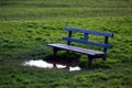 Old metal bench on the grass field and a big puddle in front of it, which makes it impossible to use. Concept photo