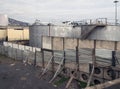 Old metal industrial storage tanks with rusty inspection ladders and valves surrounded by a corrugated steel fence and wall