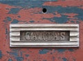 Old metal letterbox in a red wooden door with chipped peeling paint with the word cartas, translation from portuguese is mail