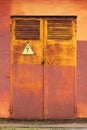 Old metal rusty grunge door to electric switchboard with high voltage arrow lightning sign in yellow triangle, abstract background Royalty Free Stock Photo