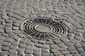 Old metal sewer hatch in the middle of the road, laid out of a smooth paving ston Royalty Free Stock Photo