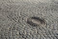 Old metal sewer hatch in the middle of the road, laid out of a smooth paving ston Royalty Free Stock Photo