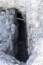 Old mining shaft into the rock timbered with rotted wood and filled with dirt and sagebrush