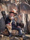Old Mongolian hunter with a golden eagle resting sitting by a ro