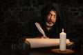 An old monk in his cell writes a message on parchment with a goose quill pen by candlelight. Royalty Free Stock Photo