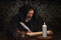 An old monk in his cell writes a message on parchment with a goose quill pen by candlelight. Royalty Free Stock Photo