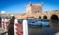 Old moroccan man standing and blue boats in ancient fort in Esaouira, Morocco