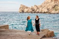 Old mother and adult daughter in retro old-fashioned clothes holding hands walking and talking on the stone beach of the blue sea