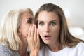 Older mother whispering in young daughter ear telling shocking n