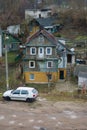 An old multi-storey wooden house in a poor area. A white car is parked near the cottage. Poor living conditions in impoverished