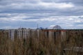 An old multi-story building stands amidst overgrown vegetation, with a dome structure in the distance Royalty Free Stock Photo