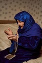 An old Muslim grandmother prays against the background of prayer with a rosary in her hands