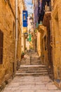 Old narrow medieval street with yellow buildings with colorful balconies in town Singlea, Valletta, Malta