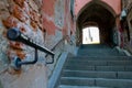 Old narrow street with shriveled brick walls, cement stairs and a black metal handrail pointing up towards an archway Royalty Free Stock Photo