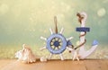 Old nautical wood wheel, anchor and shells on wooden table over abstract glitter background