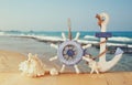 Old nautical wood wheel, anchor and shells on wooden table over sea background.