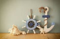 Old nautical wood wheel, anchor and shells on wooden table over wooden background. vintage filtered image