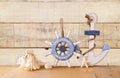 Old nautical wood wheel, anchor and shells on wooden table over wooden background. vintage filtered image