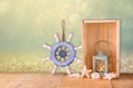 Old nautical wood wheel, lantern and shells on wooden table over wooden glitter background