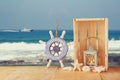 Old nautical wood wheel and shells on wooden table over sea background.