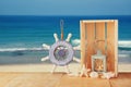 Old nautical wood wheel and shells on wooden table over sea background.