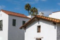 Old and new Spanish style buildings with white plaster walls and red tile roofs with palm trees under a blue sky in Santa Barbara