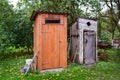 Old and next to it a renovated wooden toilet in the garden outside in the open air Royalty Free Stock Photo