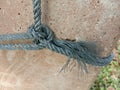 Old nylon ship ropes tied to knot bound around cement electrical post on ground flooring closeup.