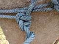 Old nylon ship ropes tied to knot bound around cement electrical post on ground flooring closeup.