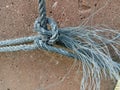 Old nylon ship ropes tied to knot bound around cement electrical post on ground flooring closeup.