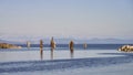 Old ocean pilings in a calm, serene ocean with a breakwater on either side and a slight pink sk