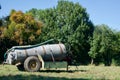 Old oil tank with pipes in it mounted on wheels in a sunny field surrounded by trees Royalty Free Stock Photo